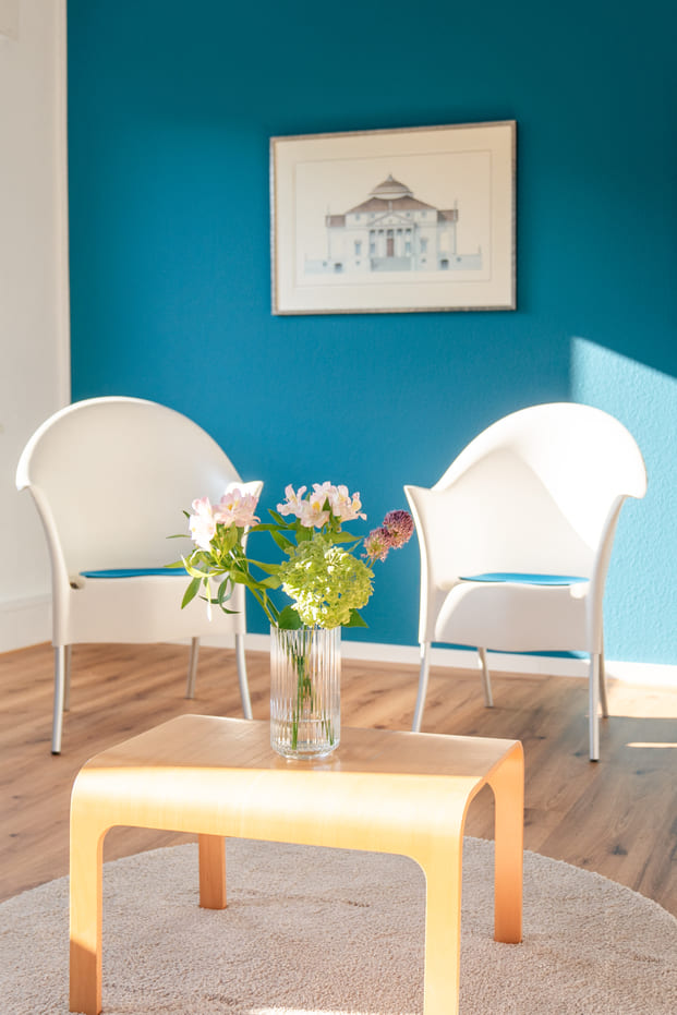 Zwei weiße Sessel und ein kleiner Holztisch mit Blumenstrauß im Gruppenraum